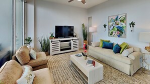 A modern living room with a flat-screen TV, two sofas, a coffee table, and decorative pillows.