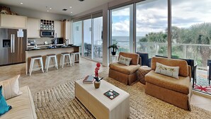 A spacious living area with a large window overlooking a balcony, a kitchen with modern appliances, and comfortable seating.