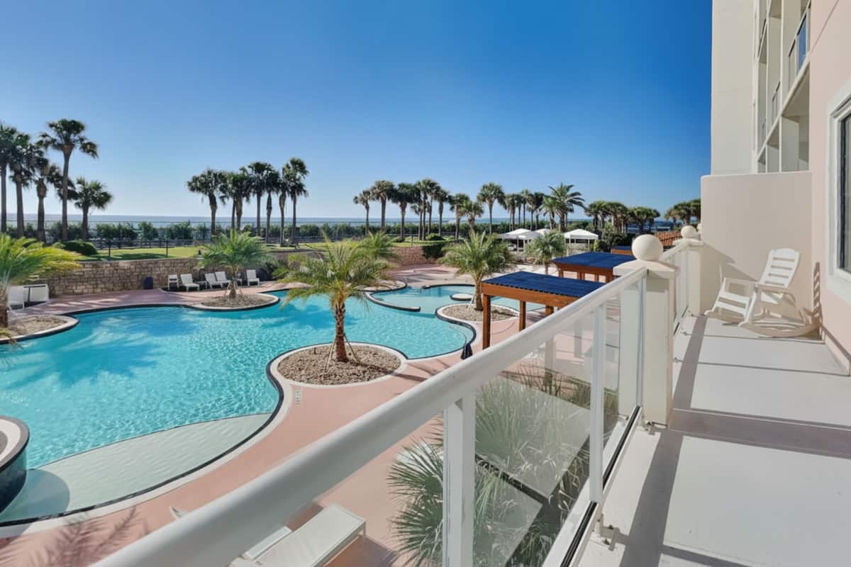 A resort pool area with multiple swimming pools, palm trees, and lounge chairs.