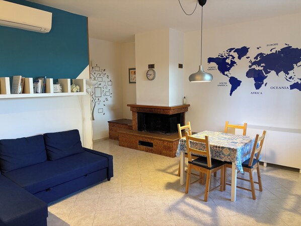 Un salon avec un canapé bleu, une table à manger avec quatre chaises, une cheminée et une carte du monde accrochée au mur.