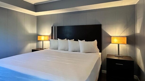 Een moderne hotelkamer met een groot bed, twee nachtkastjes en een hoofdbord met een zwart paneel.