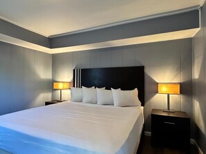 Une chambre d’hôtel moderne avec un grand lit, deux tables de chevet et une tête de lit dotée d’un panneau noir.