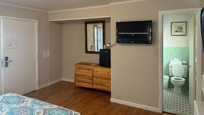 Een hotelkamer met een houten dressoir, een aan de muur bevestigde televisie, een deur naar een badkamer met toilet en wastafel, en een bed met een bedekking met een patroon.