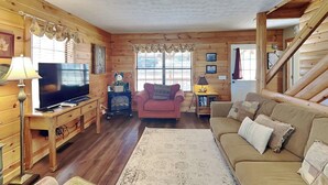 A cozy living room with wooden walls, a television, a sofa, a chair, and a rug. - Kajun Kove by Jackson Mountain Rentals (Sevierville)
