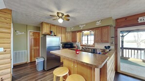 A kitchen with wooden cabinets, a stainless steel refrigerator, a microwave, and a large island with stools. - Kajun Kove by Jackson Mountain Rentals (Sevierville)