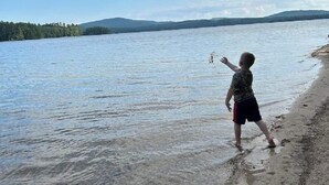Un niño jugando junto a un lago con cielo despejado y colinas al fondo.