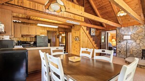 Interior de una cabaña de madera con comedor, cocina y chimenea de piedra.