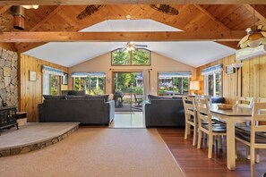 A spacious living area with a high ceiling, wooden beams, a stone accent wall, and a view of the outdoors.