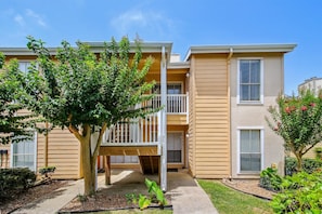 A two-story apartment building with a covered patio and a tree in the foreground.