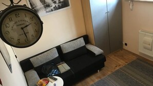 Ein Wohnzimmer mit einem schwarzen Sofa, einem kleinen weißen Tisch mit einer Fernbedienung, einer Uhr und einem gemusterten Teppich.