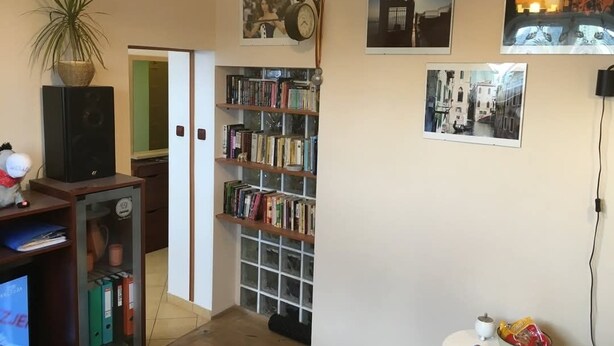 Ein Zimmer mit Bücherregal, einer Uhr und gerahmten Bildern an der Wand.