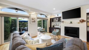 A modern living room with a large sofa, a fireplace, and a television. - Belmont Shore Retreat Rooftop Lounge, Putting Green & Near 2nd Street Beaches (Long Beach)