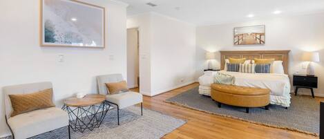 Una habitación de hotel con cama, sofá, sillón, una mesita, alfombra y obras de arte en las paredes.
