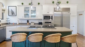 A kitchen with white cabinetry, a central island with bar stools, stainless steel appliances, and pendant lighting. - Belmont Shore Retreat Rooftop Lounge, Putting Green & Near 2nd Street Beaches (Long Beach)