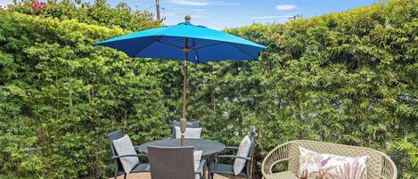 Un patio al aire libre con una mesa, sillas, un parasol azul y un sofá de mimbre.