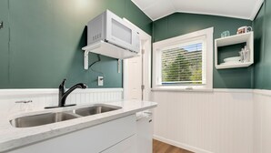 A kitchen with a double sink, white cabinets, a microwave, and a window with blinds.