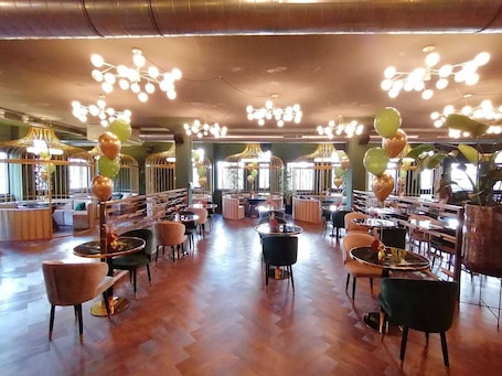 A spacious restaurant with high ceilings, modern chandeliers, and a variety of seating arrangements including round tables and cushioned chairs.