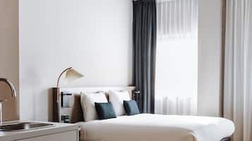 Une chambre d’hôtel moderne, équipée d’un lit, d’un bureau avec une lampe, d’une fenêtre avec des rideaux et d’un plancher en bois.