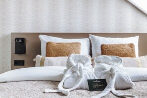 A hotel room with a neatly made bed, two white pillows, a brown woven throw, and a welcome card on the bed.