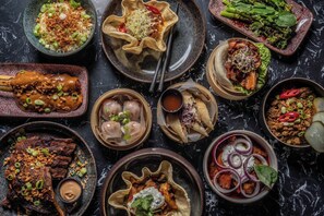 A variety of dishes including dumplings, a bowl of rice with green onions, and a plate of meat with sauce.