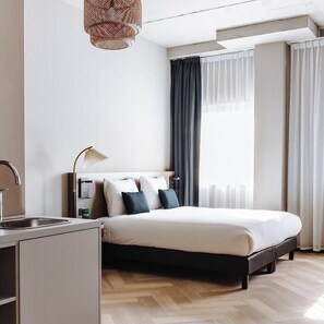 A modern hotel room with a bed, a desk with a lamp, a sink, and a large window with curtains. - Havendijk Hotel (Schiedam)