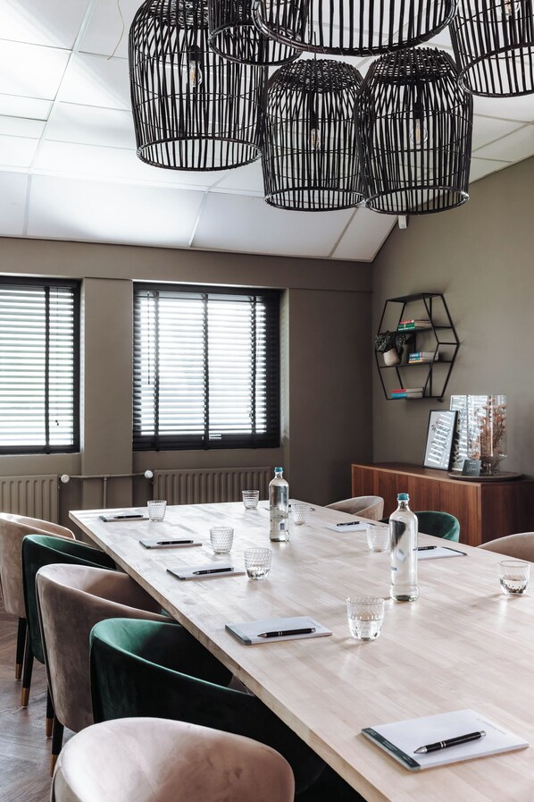 A conference room with a long table, chairs, and hanging black metal light fixtures. - Havendijk Hotel (Schiedam)