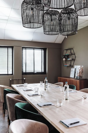 A conference room with a long table, chairs, and hanging black metal light fixtures.