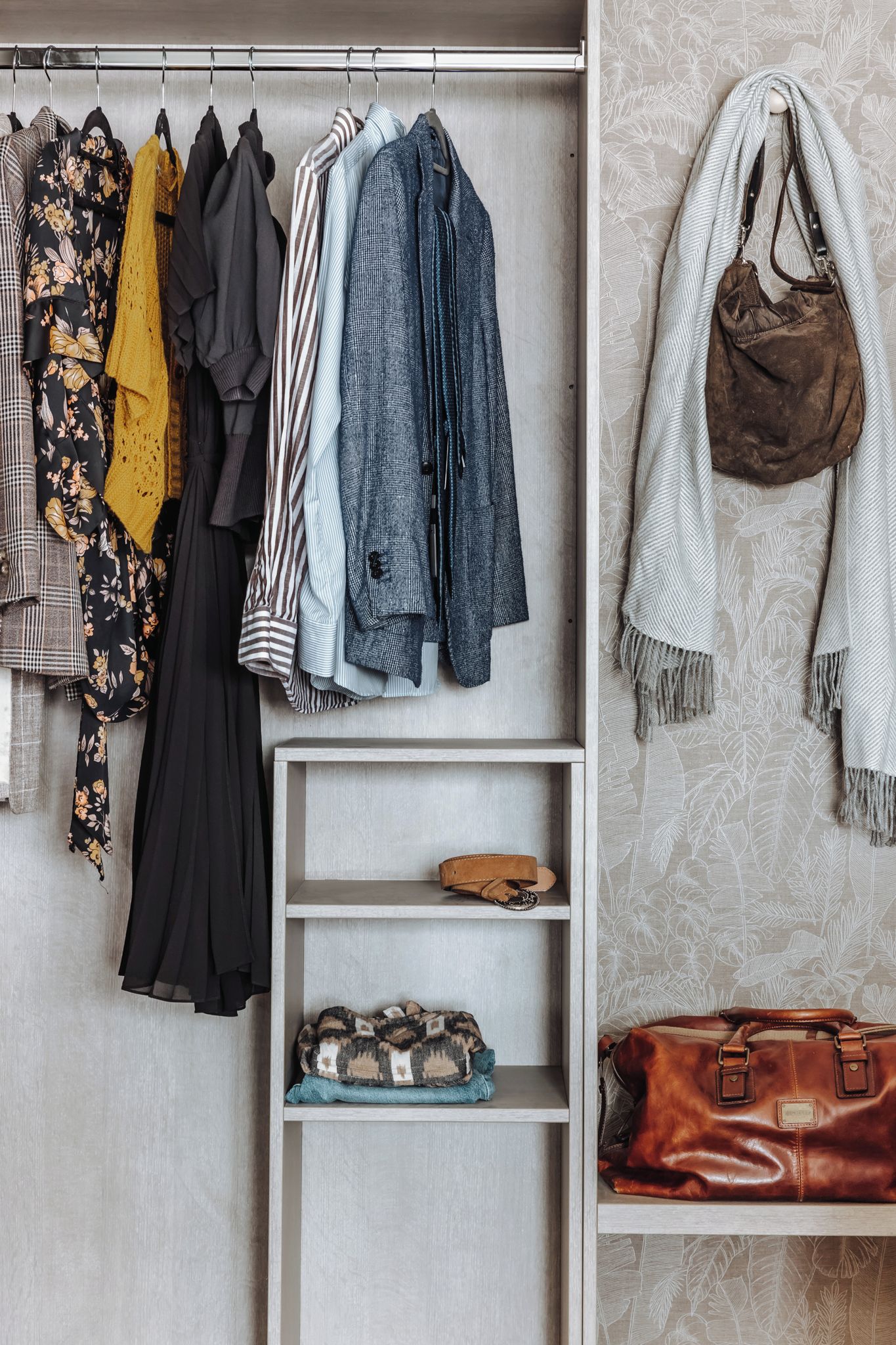 A closet with hanging clothes and shelves containing bags and shoes.