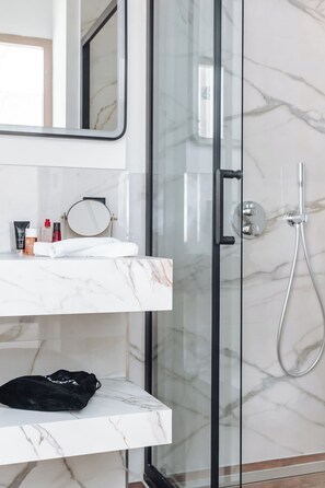 A bathroom with a glass shower door, a white marble sink, and a black bag on the counter. - Havendijk Hotel (Schiedam)