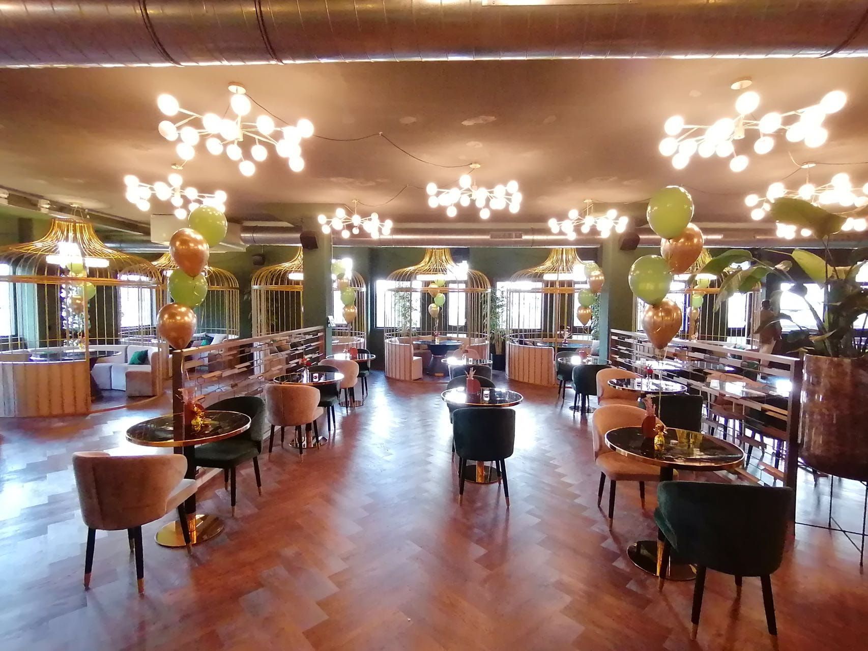 Un restaurant spacieux avec de hauts plafonds, des lustres modernes et différents types de sièges, notamment des tables rondes et des chaises rembourrées.
