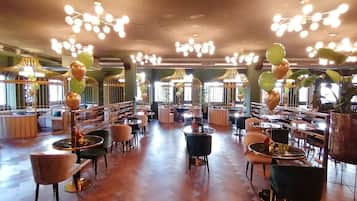 A spacious restaurant with high ceilings, modern chandeliers, and a variety of seating arrangements including round tables and cushioned chairs.