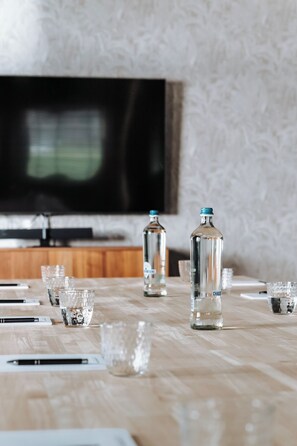 A wooden table with clear glasses, a bottle of water, and a bottle of alcohol. A television is mounted on the wall in the background. - Havendijk Hotel (Schiedam)