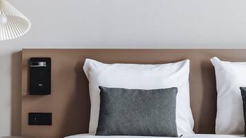 A neatly made bed with white and gray pillows, a modern headboard, and bedside controls.