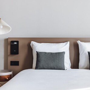 Una cama bien hecha con almohadas blancas y grises, un cabecero moderno y controles junto a la cama.