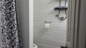 A bathroom with a white brick wall, a toilet, a towel rack, and a shower curtain with a leaf pattern. - Charming 1-bedroom apartment in amazing Wichita with WiFi, AC (Wichita)