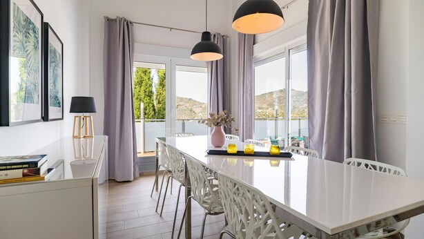 Une cuisine moderne dotée d’un grand îlot central, de chaises blanches et de luminaires suspendus.