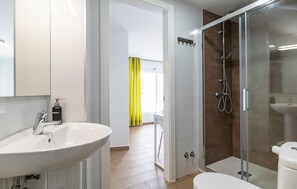 Un baño moderno con un lavabo blanco, cabina de ducha con mampara de vidrio y un inodoro.