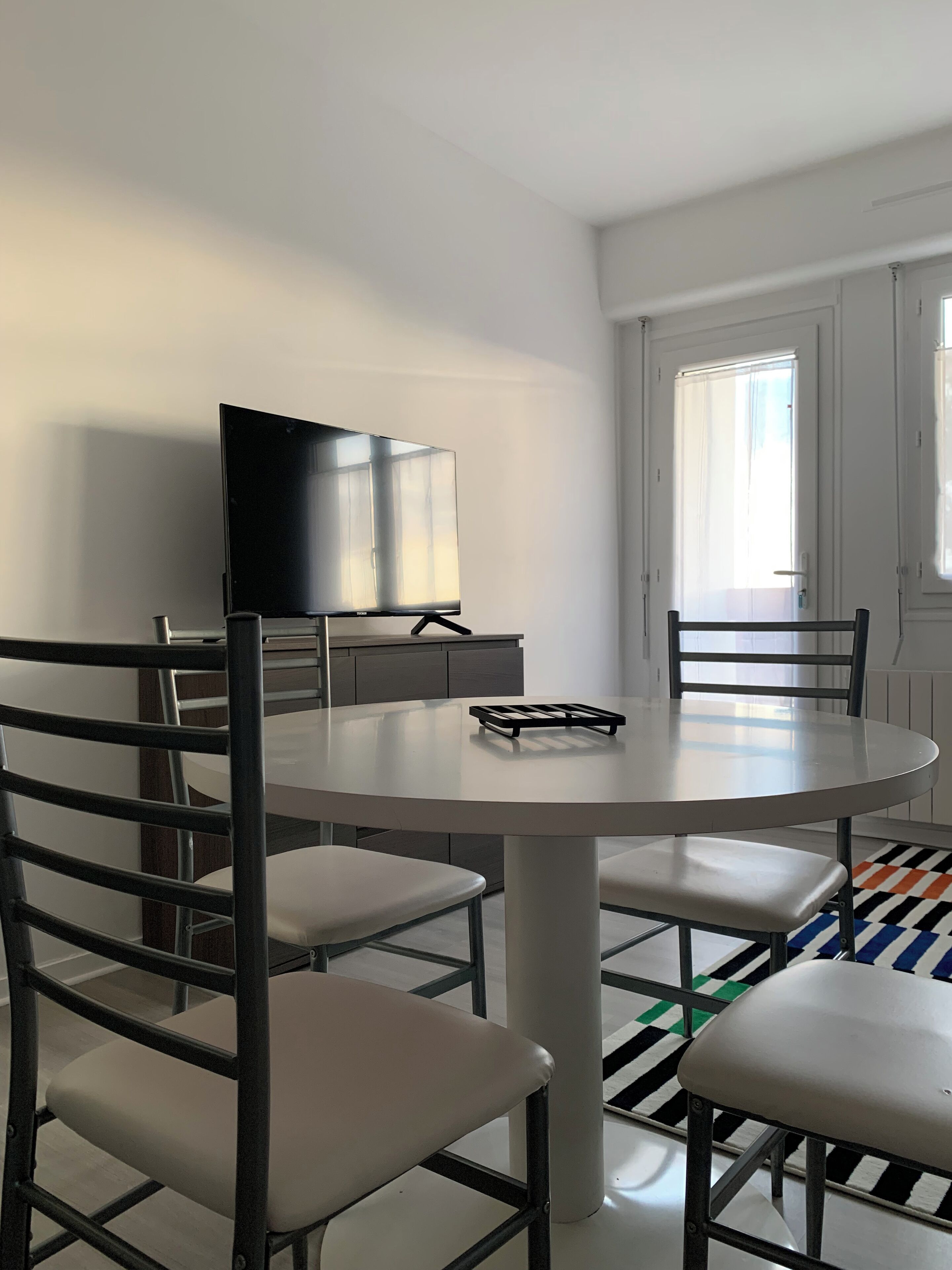 Un espace repas moderne avec une table ronde, quatre chaises, un téléviseur et un tapis à motifs.