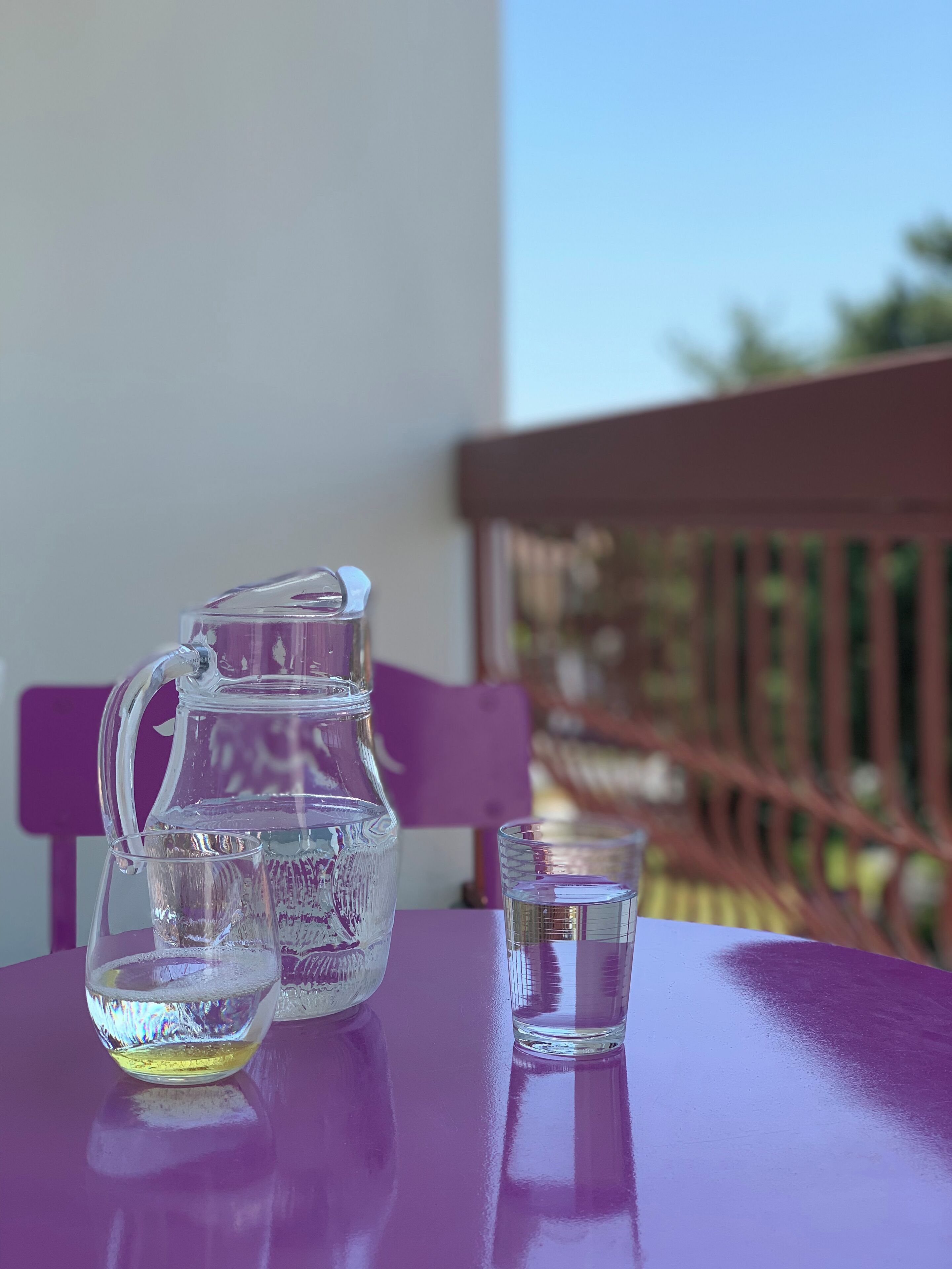 Un jarro de vidrio transparente y un vaso sobre una mesa morada.