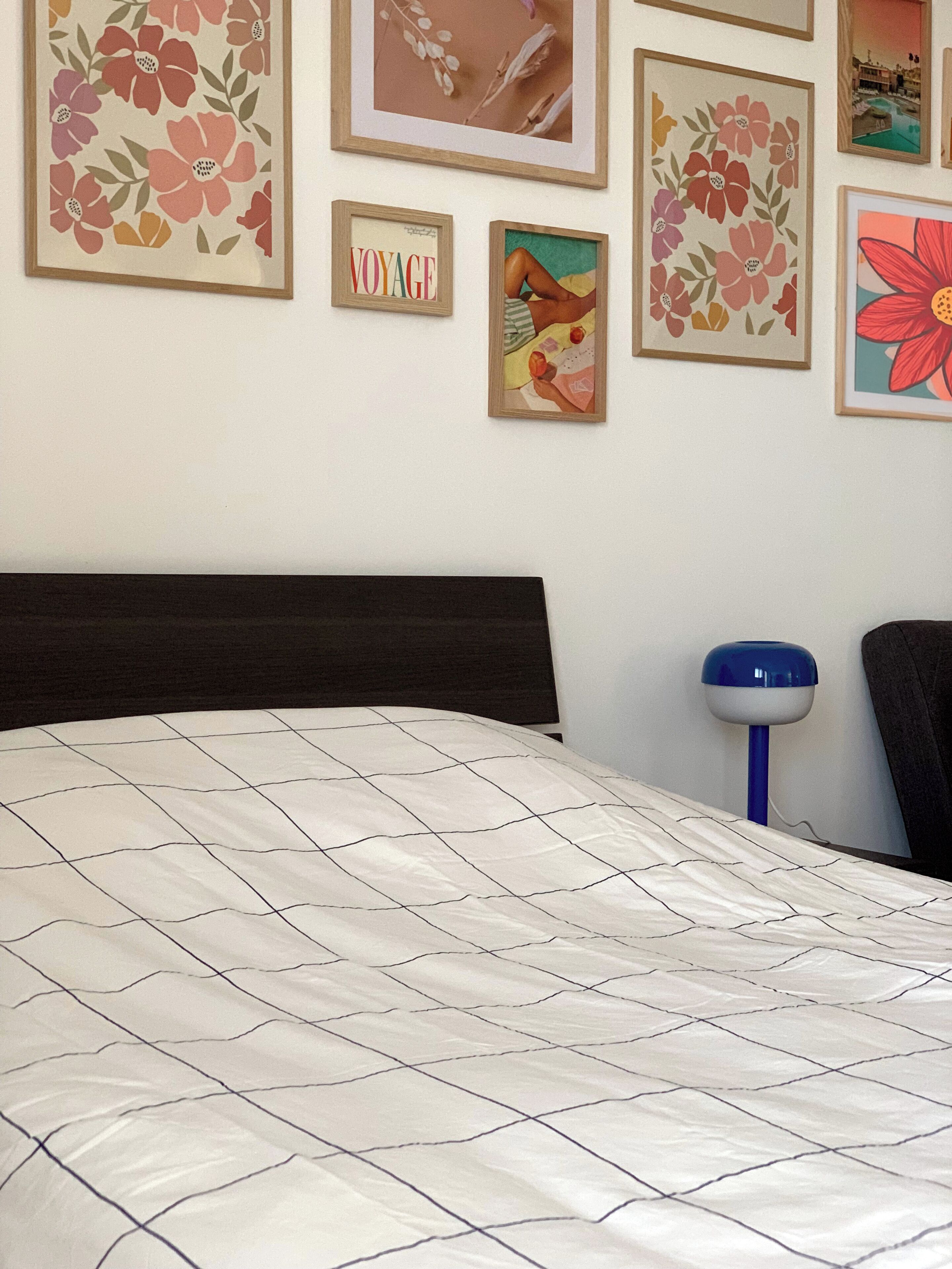 Quarto com cama, mesa de cabeceira e parede com obras de arte emolduradas.