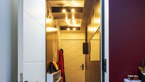 Um corredor estreito com piso de madeira, uma porta branca à esquerda e uma parede vermelha à direita.