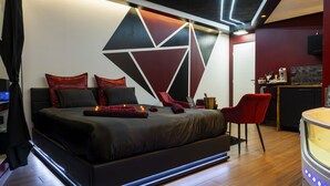 A modern bedroom with a large bed, a red chair, a small desk, and a wall with geometric patterns. - ✨Unique and romantic suite with private spa✨ (Voiron)