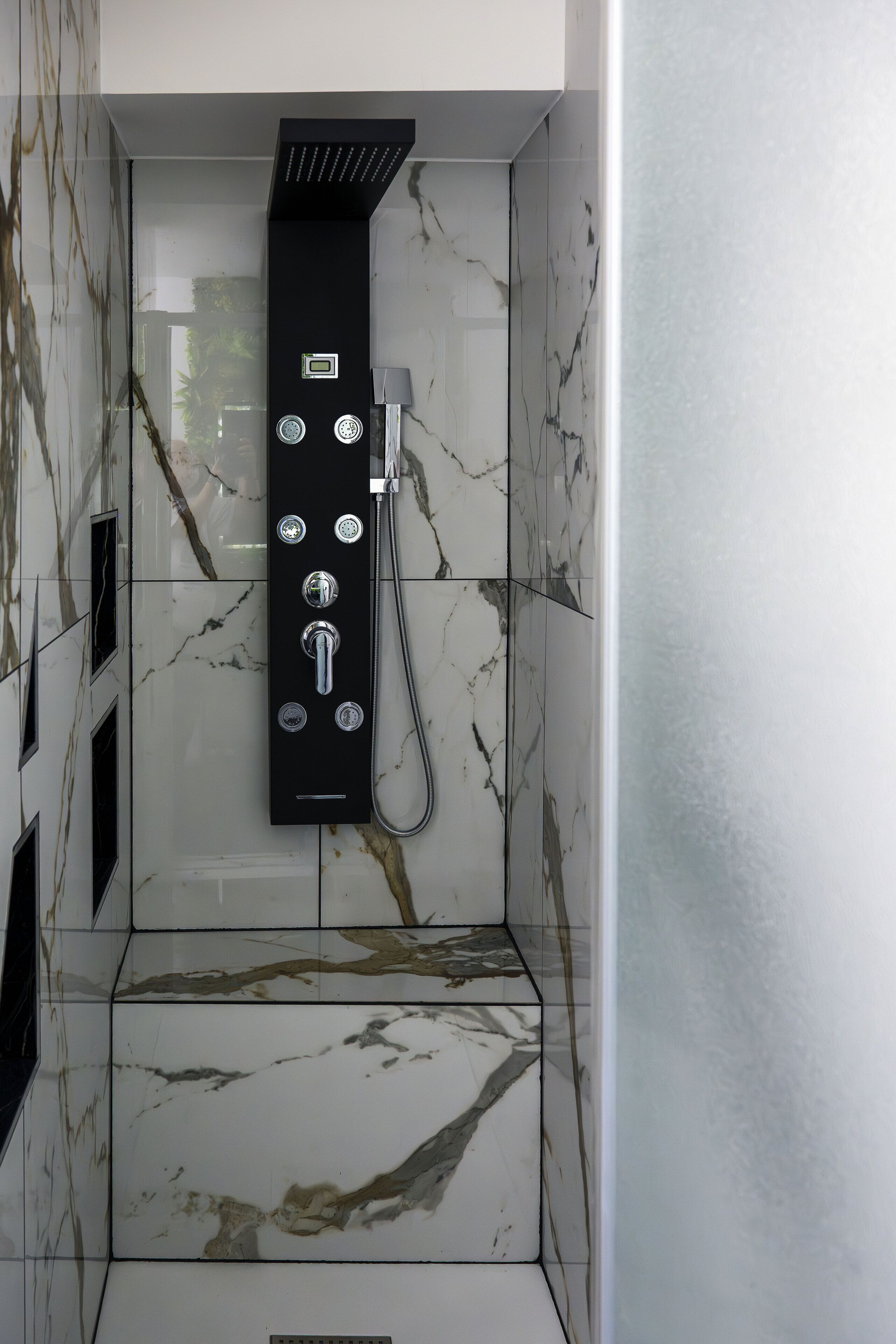 Une salle de bain moderne avec un panneau de douche noir, des carreaux de marbre et un espace de douche délimité par des parois en verre.