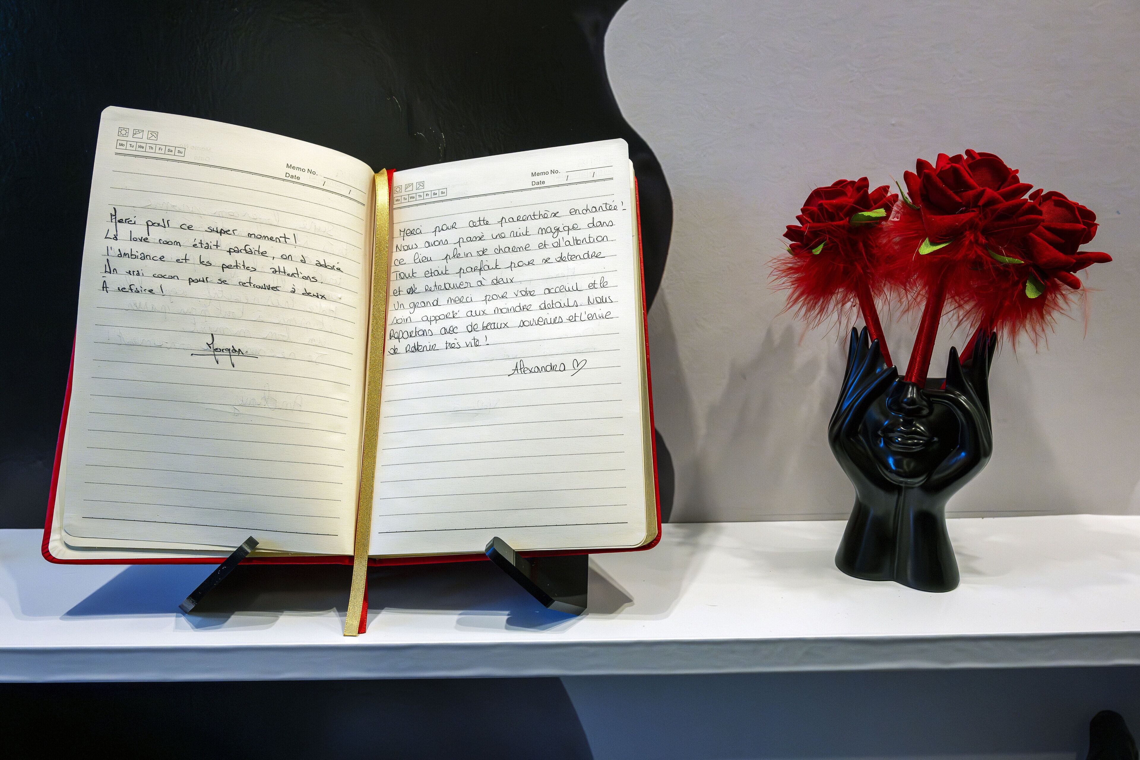 An open notebook on a stand with handwritten notes, next to a decorative vase with red flowers.