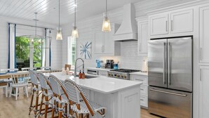 A modern kitchen with white cabinetry, stainless steel appliances, and a large island with bar stools.