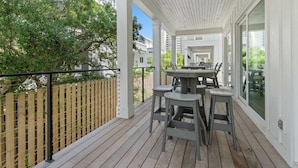A covered outdoor patio with a wooden deck, a table with chairs, and a view of a residential area.
