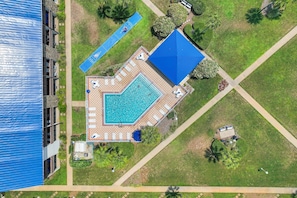Vista aérea de un resort con piscina, sillas de descanso y cancha de tenis.
