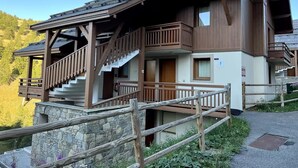Ein mehrstöckiges Chalet mit Holzbalkonen, einem Steinfundament und einer Treppe, die zu den oberen Stockwerken führt.