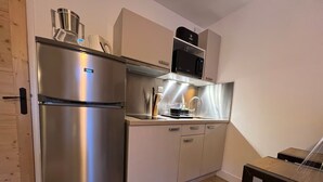 Eine kompakte Küche mit Edelstahlkühlschrank, Mikrowelle und Kaffeemaschine auf der Arbeitsfläche.