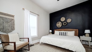 A bedroom with a bed, a chair, a window with curtains, and wall decor.